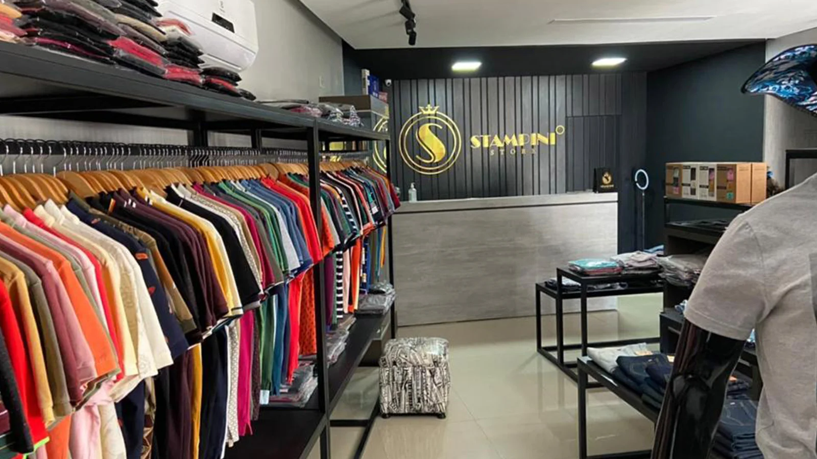 Interior da loja Stampini Store, com araras de roupas e recepção